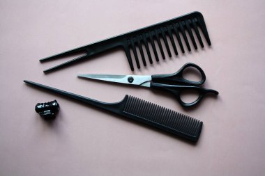 Bir kuaför için alet takımı. Siyah makas ve pembe arka planda bir tarak..