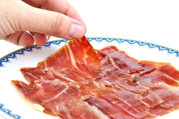 Mans hand met een Spaanse serrano ham segment. — Stockfoto