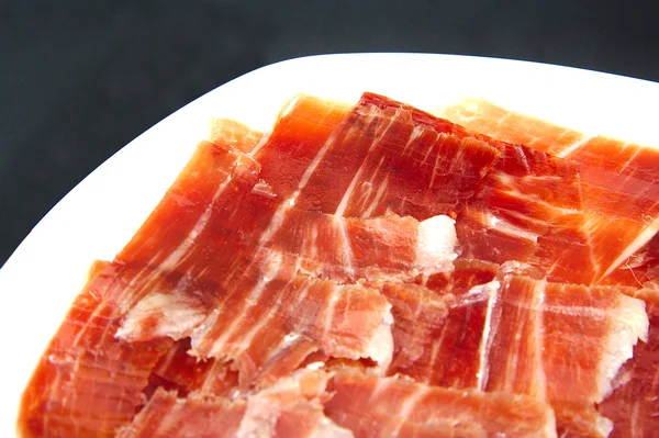 Closeup of spanish serrano ham on black background. — Stock Photo, Image