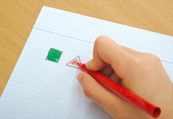 Niño dibujando triángulo rojo y cuadrado verde con crayones en el aula. Concepto escolar . — Foto de Stock
