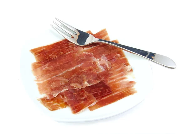 Serrano ham on a white dish with a metal fork. Jabugo. Spanish tapa. — Stock Photo, Image