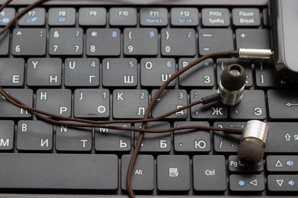 Auriculares y teléfono celular en el teclado . —  Fotos de Stock