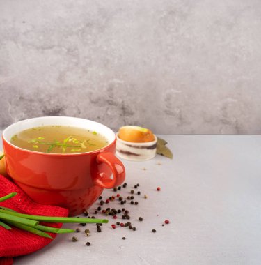 Kırmızı peçete ve yeşil soğanlı kırmızı kasede kolajen ve amino asitlerle ev yapımı sığır eti çorbası, siyah bezelye, doğranmış beyaz soğan ve gri arka planda havuç. Bağışıklık sistemi ve fonksiyonel bileşenleri destekle