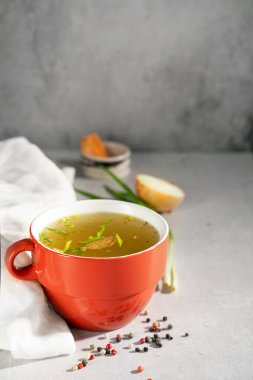 Kırmızı peçete, yeşil soğan, doğranmış beyaz soğan ve gri arka planda havuç içeren kırmızı kasede kolajen ve amino asitlerle ev yapımı et kemiği çorbası. Bağışıklık sistemi ve işlevsel bileşenleri destekleyin.