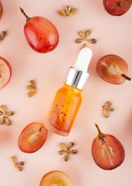 Evde cilt bakımı için cam şişenin içine üzüm tohumu yağı konsepti koy. Pembe arka planda taze üzüm ve çekirdekli yaratıcı modern düz kompozisyon. Doğanın kanunu. Kapat..