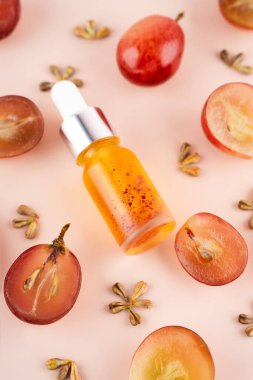 Evde cilt bakımı için cam şişenin içine üzüm tohumu yağı konsepti koy. Pembe arka planda taze üzüm ve çekirdekli yaratıcı modern düz kompozisyon. Doğanın kanunu. Kapat..