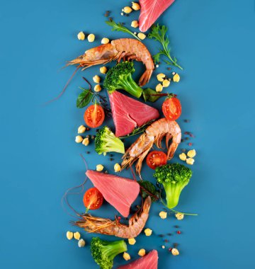 Parlak mavi arka planda karides, ton balığı, brokoli, kiraz domates ve nohut. Sağlıklı Pescataian diyeti kavramı. Deniz ürünleri, balık, sebzeler. Pescetarian ve Flexsitarian diyet ürünleri. Üst görünüm.