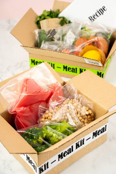 Online Home Food Delivery. Craft Box with packed tuna, shrimp, vegetables and recipe card on a kitchen background. Food delivery services during coronavirus pandemic and social distancing