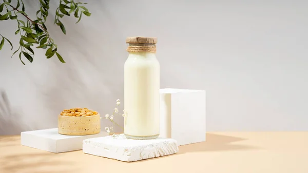 Vegetable pea milk in a bottle and peas in handmade ceramic bowl on white podium, pedestal on beige background. shadows from green foliage.Gluten-free, lactose-free vegan product. Modern. Copy space