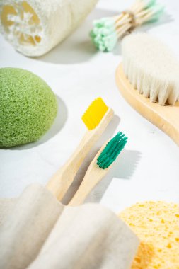 Doğal ekolojik banyo aksesuarları: ahşap tarak, bambu diş fırçası, masaj fırçası, kulak çubuğu, mermer zemin üzerinde konyak süngeri. Sıfır atık etik ürün. Yaklaş, düz yat, üst manzara.