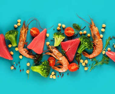 Parlak mavi arka planda karides, ton balığı, brokoli, kiraz domates ve nohut. Sağlıklı Pescataian diyeti kavramı. Deniz ürünleri, balık, sebzeler. Pescetarian ve Flexsitarian diyet ürünleri. Üst görünüm..