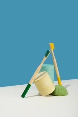 Modern natürmort. Isometric diagonal projeksiyon. Geometrik sarı şekiller, ayağa kalkın. Bambu diş fırçası. Sıfır atık, pastel mavi ve pembe arka plan. Çevre dostu, sürdürülebilir yaşam tarzı.