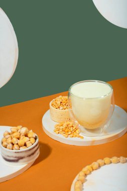 Şişede sebze sütü, beyaz podyumda bezelye kabı, bej yeşil arka planda kaide. Gölgeler. Glüten ve laktoz içermeyen vejetaryen ürünleri. Modern kompozisyon.