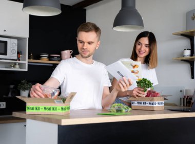 Mutlu Kafkasyalı beyaz çift çevrimiçi ev yemeği dağıtımı yapıyor. İçinde ton balığı, karides, sebze ve yemek tarifi olan bir kutu. Yemek dağıtım servisi. Restorandan akşam yemeği..