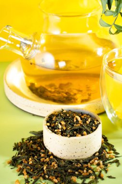 Japanese green tea Genmaicha.Tea leaves with fried brown rice on a bright yellow background with a shadow.Slimming trend tea concept. a cup of tea. brew a transparent teapot clipart