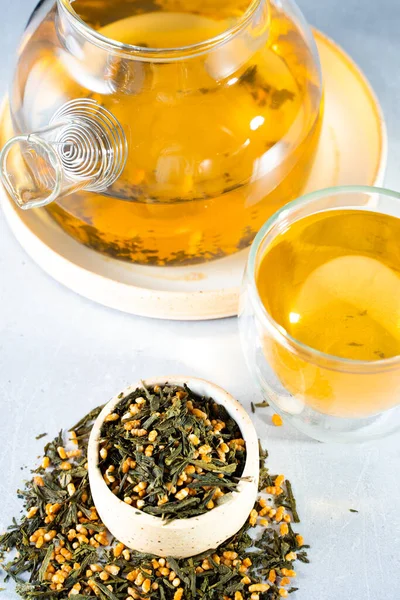 Chá verde japonês Genmaicha.Chá folhas com arroz integral frito em um fundo cinza brilhante com um conceito de chá tendência shadow.Slimming. uma chávena de chá. brew um bule transparente — Fotografia de Stock