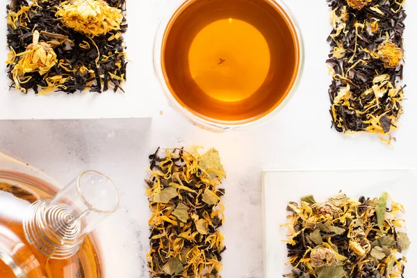 Ένα φλυτζάνι τσάι με βότανα. και ζεστή γυάλινη τσαγιέρα με λουλούδια καλέντουλας σε λευκό βάθρο. Γύψινο, μοδάτο βάθρο. Να ηρεμήσουν τα ποτά. Οριζόντια — Φωτογραφία Αρχείου