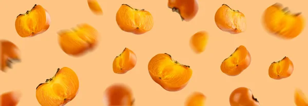 Frutta fresca arancione galleggiante variopinta intera e affettata di cachi biologici con foglie su fondo pesca. Note di alimentazione e concetto di cibo. Levitazioni cibo. Layout creativo per elemento di design. Bandiera — Foto Stock