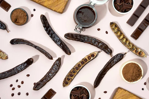 Organic carob pods, powder and carob molasses on a beige background, locust bean healthy food, Ceratonia siliqua harnup. Natural vegan eating. Creative food pattrern. Flat lay.Top view