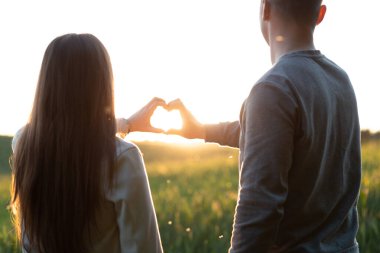 Günbatımı gökyüzünün arka planında aşıkların kalp şekli.