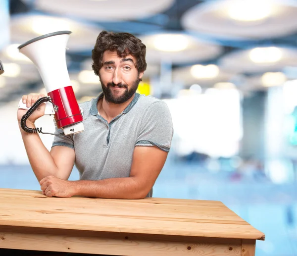 Gek jonge man aan tafel met megafoon — Stockfoto