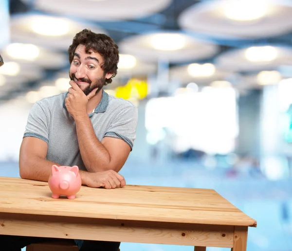 Crazy young man at table with piggybank — Stock Photo, Image