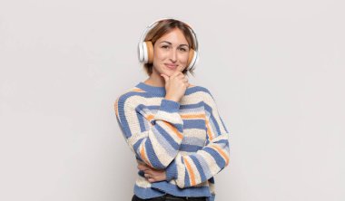 Genç sarışın kadın mutlu, kendinden emin bir ifadeyle gülümsüyor elleri çenesinde, merak ediyor ve yan tarafa bakıyor.