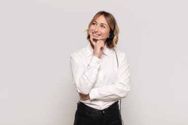 Genç sarışın kadın mutlu bir şekilde gülümsüyor ve hayal kuruyor ya da şüphe ediyor.