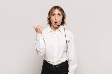 Genç sarışın kadın inançsızlıktan şaşkın şaşkın bakıyor, yan taraftaki objeyi işaret ediyor ve diyor ki: