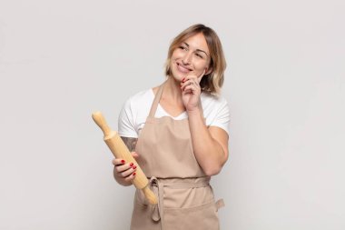 Genç sarışın kadın mutlu bir şekilde gülümsüyor ve hayal kuruyor ya da şüphe ediyor.