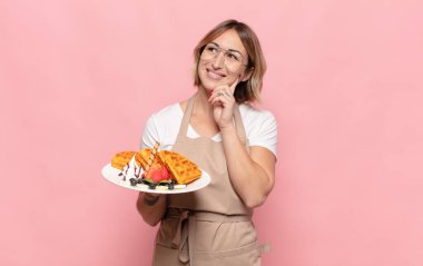 Genç sarışın kadın mutlu bir şekilde gülümsüyor ve hayal kuruyor ya da şüphe ediyor.