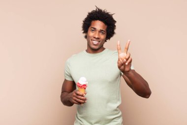 Genç siyah afro adam gülümsüyor ve arkadaş canlısı görünüyor, iki ya da iki numarayı gösteriyor, eli önde, geriye doğru sayıyor.