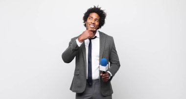 Genç siyah afro adam mutlu bir şekilde gülümsüyor ve hayal kuruyor ya da şüphe ediyor.