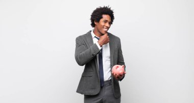 Genç siyah afro adam mutlu, kendinden emin bir ifadeyle gülümsüyor, çenesinde elleri, merak ediyor ve yan tarafa bakıyor.