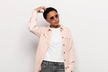 Genç siyah afro kadın şaşkın ve şaşkın hissediyor, başını kaşıyor ve yana bakıyor.