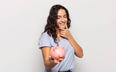 Genç İspanyol kadın mutlu, kendinden emin bir ifadeyle gülümsüyor, çenesinde elleri, merak ediyor ve yan tarafa bakıyor.