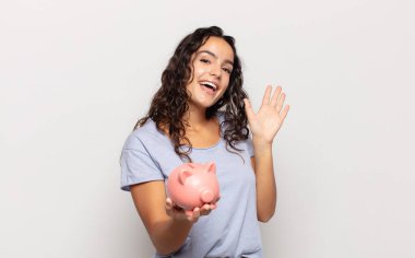 Genç İspanyol kadın mutlu ve neşeyle gülümsüyor, el sallıyor, sizi selamlıyor ya da veda ediyor.