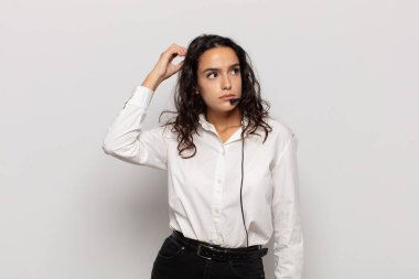 Genç İspanyol kadın şaşkın ve şaşkın hissediyor, kafasını kaşıyor ve yan tarafa bakıyor.