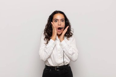 Genç İspanyol kadın şok olmuş ve korkmuş hissediyor, ağzı açık ve elleri yanaklarında korkmuş görünüyor.
