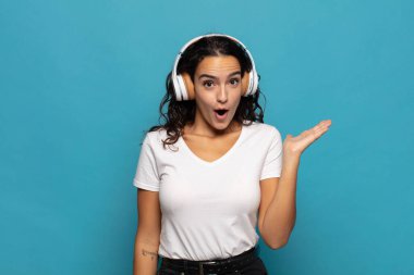 Genç İspanyol kadın şaşırmış ve şoka uğramış görünüyor, çenesi düşmüş, eli açık bir objeyi tutuyor.