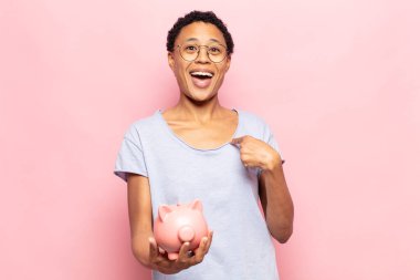 Genç siyah afro kadın mutlu, şaşkın ve gururlu hissediyor, heyecanlı ve şaşkın bir bakışla kendini işaret ediyor.