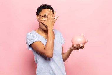 Genç siyah afro kadın şok olmuş, korkmuş ya da korkmuş görünüyor. Yüzü elle kaplanmış ve parmaklarının arasından gizlice bakıyor.