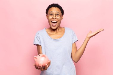 Genç siyah afro kadın mutlu, heyecanlı, şaşırmış ya da şok olmuş hissediyor, gülümsüyor ve hayrete düşüyor.