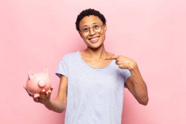 Genç siyah afro kadın neşeyle gülümsüyor, mutlu hissediyor ve yan ve yukarı doğru işaret ediyor, fotokopi uzayındaki nesneleri gösteriyor.
