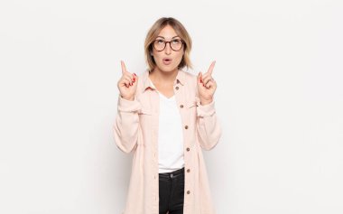 Genç ve güzel bir kadın huşu içinde ve ağzı açık bir şekilde şaşkın ve şaşkın bir bakışla yukarıya bakıyor.