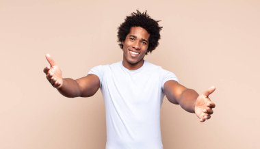 Genç siyah afro adam ciddi görünüyor ve parmaklarını dudaklarına bastırıp sessizlik ya da sessizlik talep ediyor, sır saklıyor.