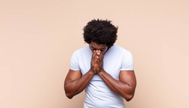 Genç siyah afro adam omuz silkiyor, kafası karışık ve kararsız, kolları bağlı ve şaşkın görünüyor.