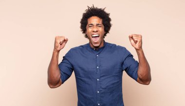 Genç siyah afro adam mutlu ve arkadaş canlısı görünüyor, gülümsüyor ve sana olumlu bir tavırla göz kırpıyor.