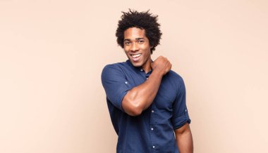 Genç siyah afro adam kendini mutlu hissediyor ve gülümsüyor. Elinde tuttuğu bir nesneye ya da konsepte bakıyor.