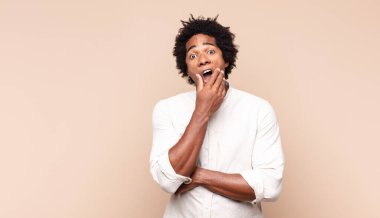 Genç siyah afro adam ağzı ve gözleri sonuna kadar açık ve eli çenesinde, nahoş bir şok hissediyor, ne ya da wow diyor